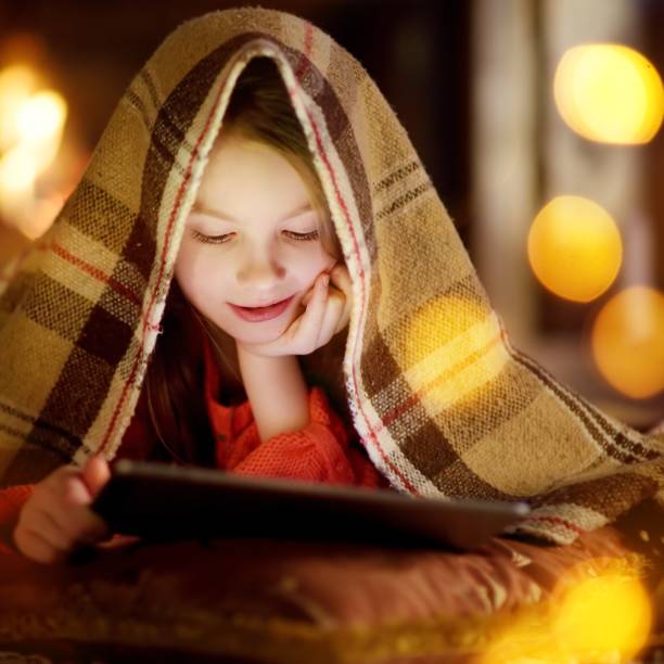 istock Adorable little girl using a tablet pc by a fireplace on Christmas evening 871285516