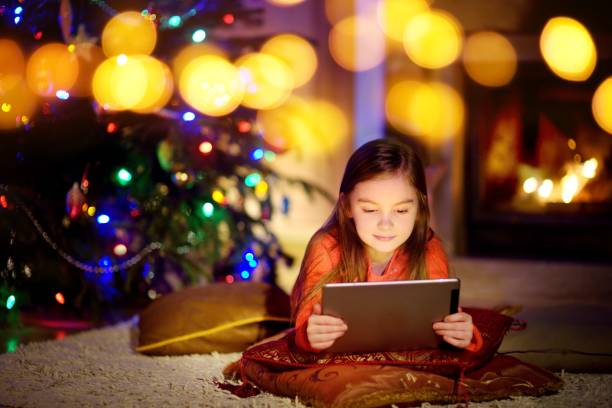 istock Adorable little girl using a tablet pc by a fireplace on Christmas evening 871285582