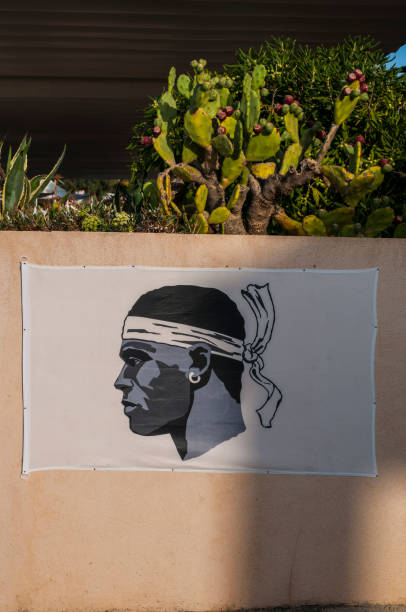 Corsica: the Flag of Corsica, a Moor's Head in black wearing a white bandana above his eyes and knotted on the back, hanging on a pink wall in the village of Centuri Port Corsica, France, Europe - August 29, 2017: the Flag of Corsica, a Moor's Head in black wearing a white bandana above his eyes and knotted on the back, adopted in 1755, hanging on a pink wall in the village of Centuri Port corsican flag stock pictures, royalty-free photos & images