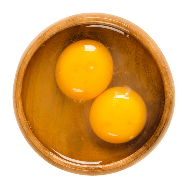 Two raw chicken eggs cracked into a wooden bowl Two raw chicken eggs cracked into a wooden bowl. Yolk and white without eggshells. Common food and versatile ingredient in cooking. Isolated macro food photo close up from above on white background. egg yolk stock pictures, royalty-free photos & images