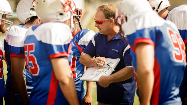 Football Head Coach Football coach going over play to football players. american football game plan stock pictures, royalty-free photos & images