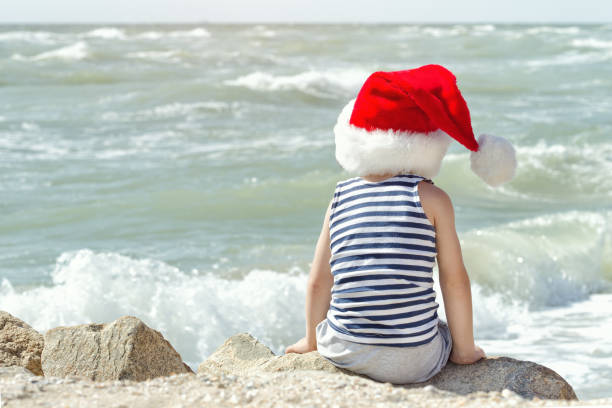 istock Kid in Santa hat sitting on the beach. Back view 871311630