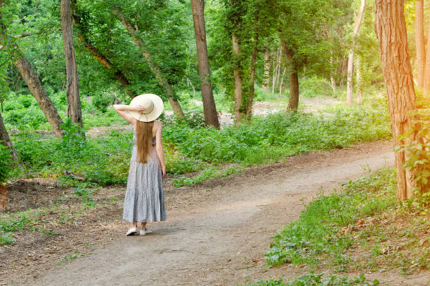 istock Girl in a hat is standing in a forest on a path in the forest. Back view 871311976