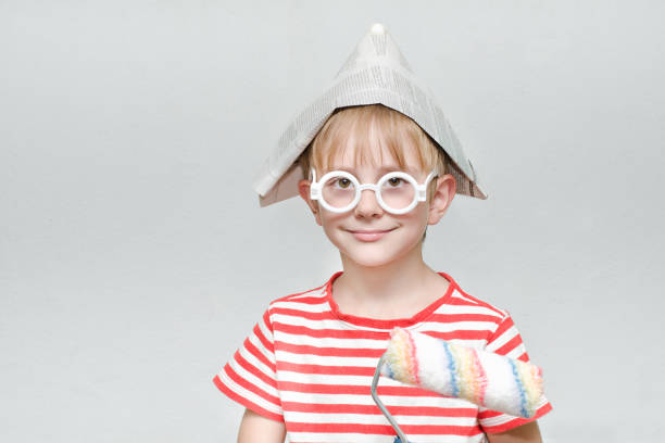 Boy in a paper hat is playing in a painter. Portrait. Roller for painting