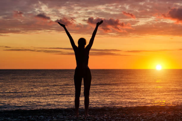 istock Girl standing hands up on the beach at sunset. Silhouette 871315724
