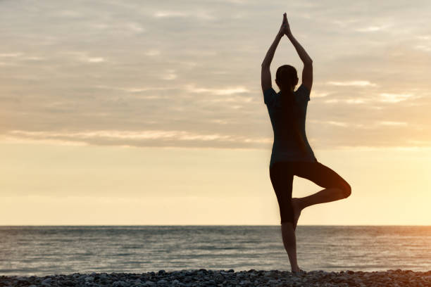 istock Girl at sunset practicing yoga at the seashore, back view 871315860