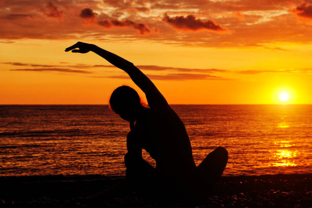 istock Girl practicing yoga on the beach. View from the back, sunset, silhouettes 871315874