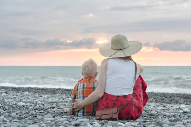 istock Mom and son sitting on the ocean shore. View from the back 871315924