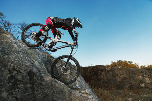 young rider on mtb bike coming down from a cliff against a blue sky stock photo