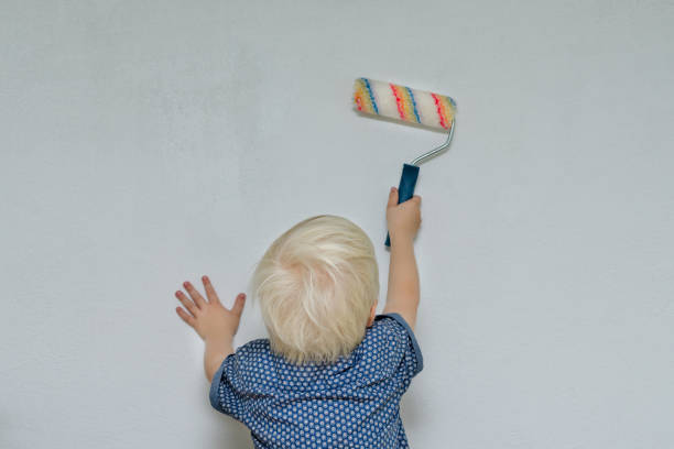 istock Small blond boy paints a wall with a roller. View from the back 871316854