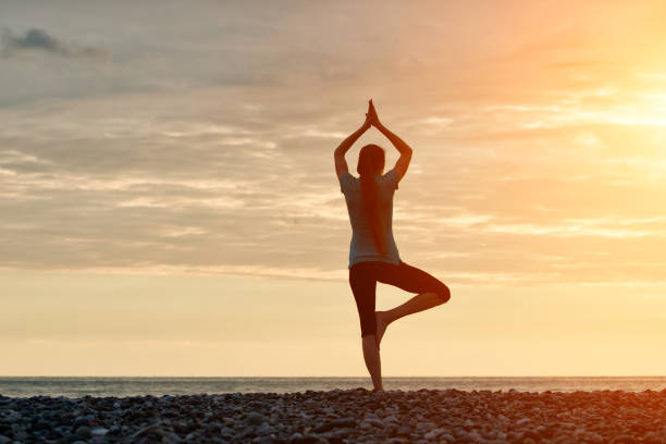 istock Girl at sunset practicing yoga at the seashore, back view 871319406