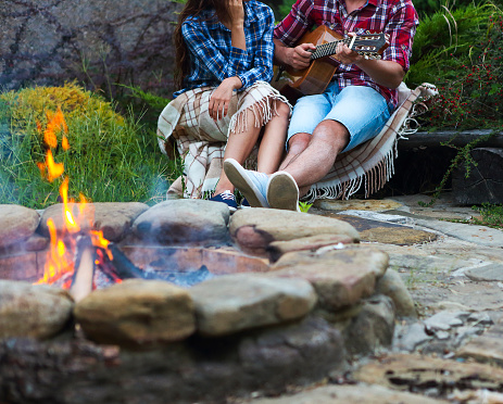 Young couple with guitar near fire outdoors. Travel and vacation concept
