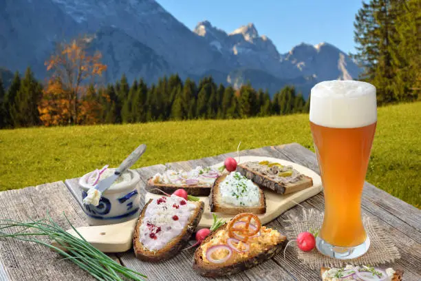 A fresh snack with different kinds of spreads on farmhouse bread served with a fresh yeast wheat beer on an old wooden table in the Bavarian Alps near to Garmisch-Partenkirchen.