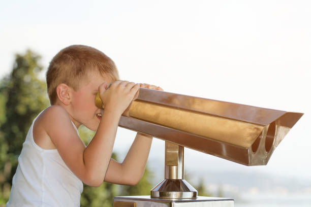 istock Boy looks at the big binoculars. Sky on background 871332522