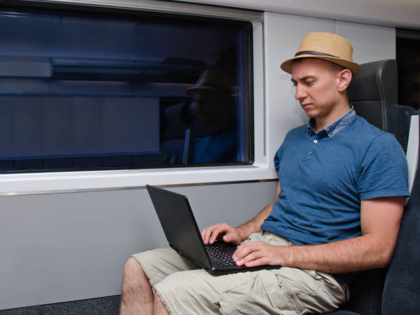 istock Young man in a hat working behind a laptop sitting in a train chair 871332764