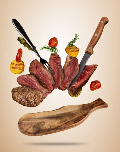 istock Flying beef steaks with grilled vegetable served on wooden cutting board. 871339710