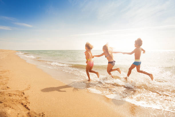 istock Kids holding hands and running along sandy beach 871342818