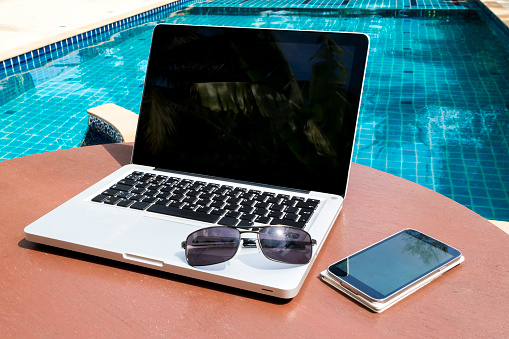 Laptop and smartphone with sunglasses on the table near the pool