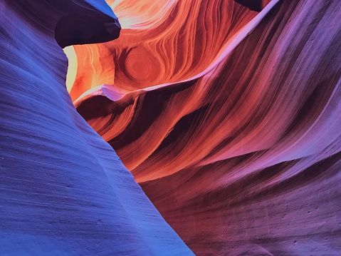 Waves in the Navajo sandstone rock in Lower Antelope Canyon in Arizona, USA were carved over time by flash floods. The light paints the rock in colorful hues of orange and purple. Image taken on a mobile device.