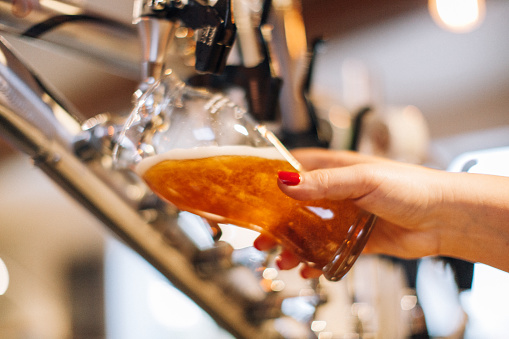 Woman pouring a glass of beer. Close-up on the hand and tap. Microbrewery