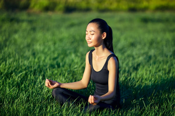 atrakcyjna azjatka siedząca na trawie w medytacji - zen like nature breathing exercise sitting zdjęcia i obrazy z banku zdjęć