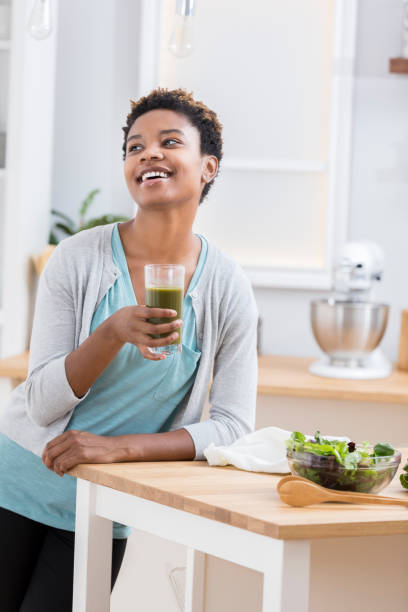 istock Young woman enjoys vegetable juice in kitchen 871381552