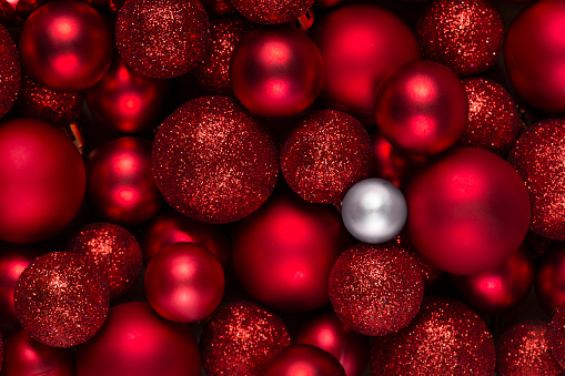 Red Christmas ornaments. One different white Christmas ball among a large group of red baubles. The difference, contrast concept. Full frame. Top view