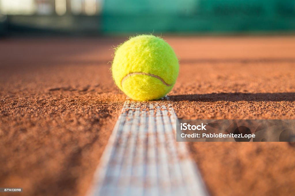 Tennis ball on white line Small tennis ball lying on white line on tennis court on sunny day. Tennis Stock Photo