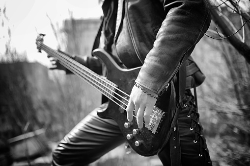 Rock guitarist on the steps. A musician with a bass guitar in a leather suit. Metalist with a guitar on the background of industrial step.