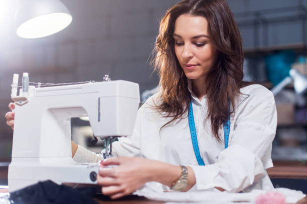 jeune designer de mode féminine sur machine à coudre dans un atelier de travail - machine sewing white sewing item photos et images de collection
