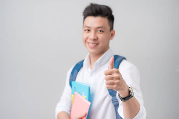 istock Asian male student making a thumb up sign isolated on gray background 871471018