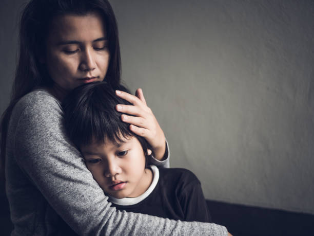 悲しい男の子が彼の母を自宅で抱きしめています。親子関係、愛と絆のコンセプトです。 - child beauty mother little boys ストックフォトと画像