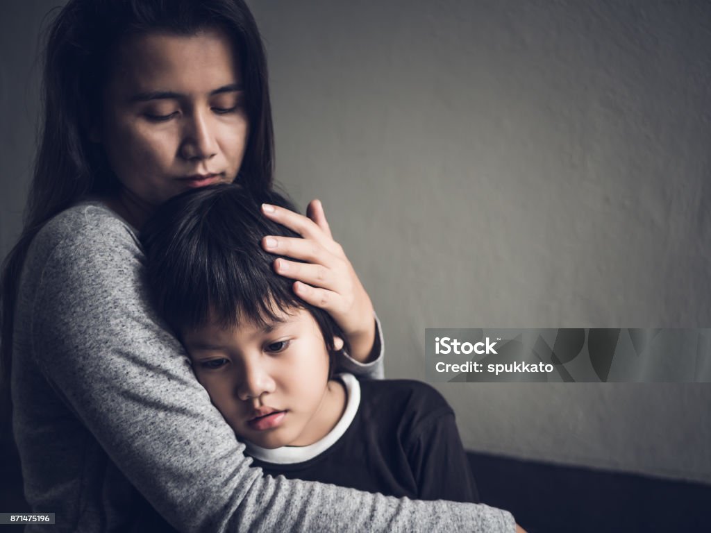 Menino triste ser abraçado por sua mãe em casa. Conceito de paternidade, amor e União. - Foto de stock de Tristeza royalty-free