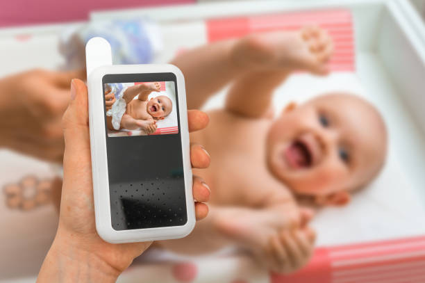 Mother is holding baby monitor camera for safety of her baby stock photo