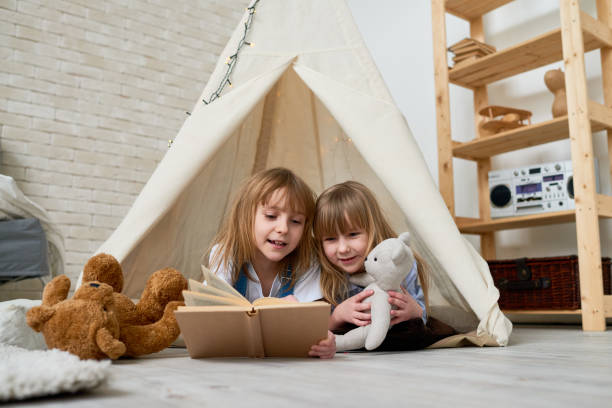 istock Cute sisters reading fairy tale in teepee 871486146