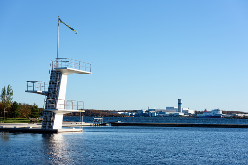 Karlskrona: Documentary of everyday life and environment.  Outdoor diving platform at Stumholmen beach with Industry and ferry terminal in background.