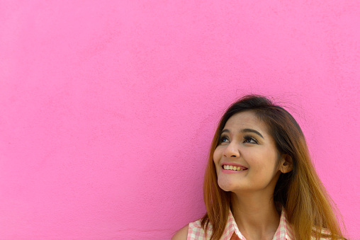 Portrait of young beautiful Asian tourist woman against pink concrete wall in Málaga, Spain