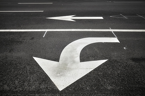 Turn or go straight street signs on asphalt, arrow pointing at viewer, conceptual background with focus on the first arrow.