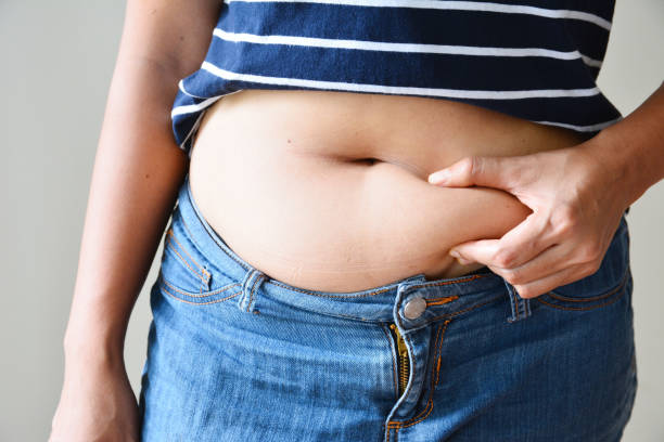 las mujeres de grasa corporal con la mano que sostiene la grasa del vientre excesivo - abdomen humano fotografías e imágenes de stock