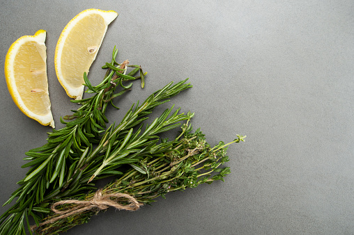 Fresh rosemary, thyme and two slices of lemon on a gray stone table.