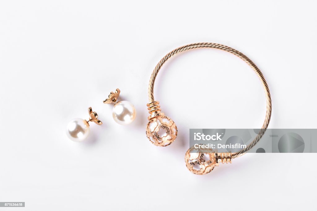 Female earings and bracelet on white background. Female earings and bracelet on white background. Earings with pearl and bangle, white background. Woman bijouterie isolated on white background. Jewelry Stock Photo