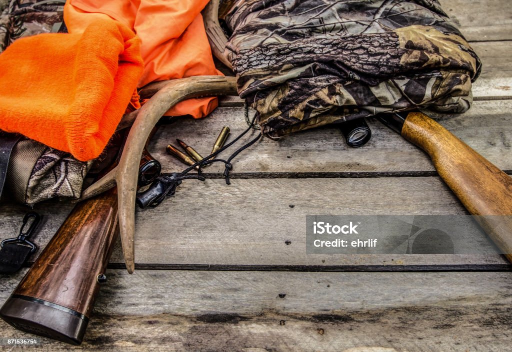 Deer Hunting Gear Background With Rifles, Rattling Antlers, Deer Call And Camouflage Deer hunting background with hunting gear and apparel on a rustic wooden background with copy space. Hunting - Sport Stock Photo