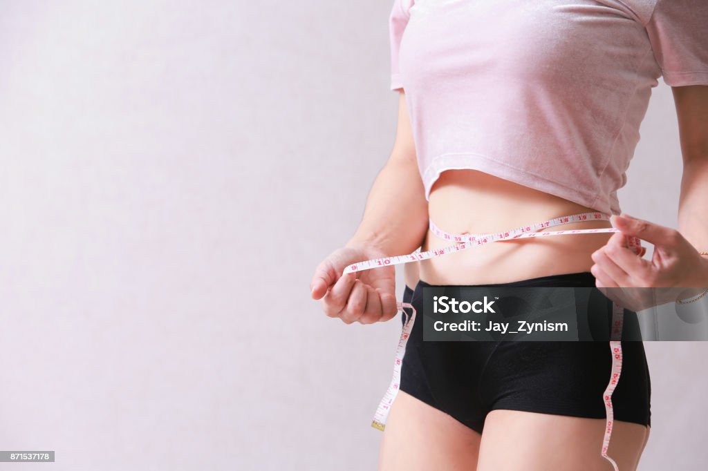 Woman measuring her slim body isolated on background. Dieting Stock Photo