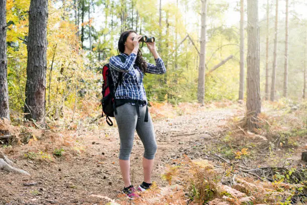 Young female hiker watching through binoculars wild birds