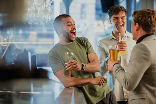 Three male friends are enjoying themselves at the bar after work, drinking pints of lager.