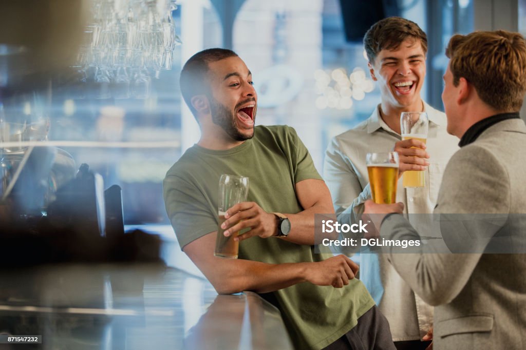 Enjoying Drinks After work Three male friends are enjoying themselves at the bar after work, drinking pints of lager. Friendship Stock Photo