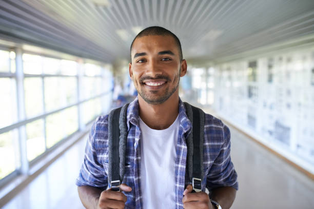 Here to secure my future Portrait of a happy young man standing in a corridor on campus backpack photos stock pictures, royalty-free photos & images