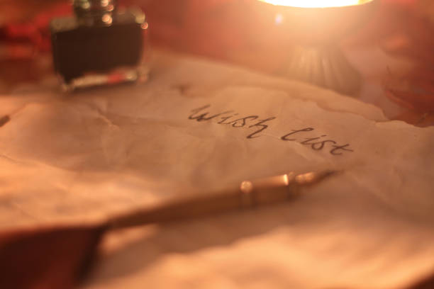 Old wishlist with feather pen and ink and candle on wooden table stock photo