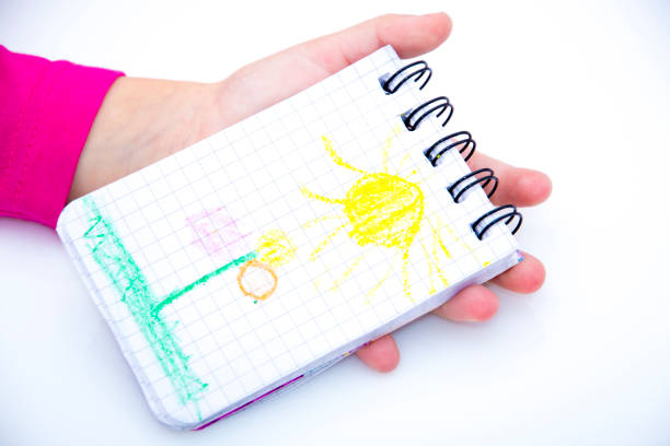 children's hands hold notebook with a painted sun. isolated.