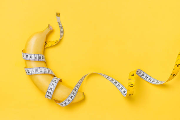 diet, fitness and health concept presented by yellow banana wrapped in measure tape isolated on yellow paper background - dieting healthy eating healthy lifestyle tape measure imagens e fotografias de stock